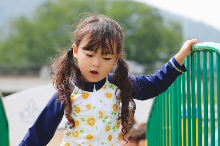 asian girl walking beside green fence