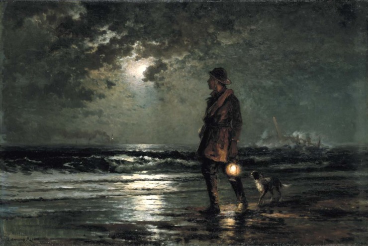 man holding a lantern walks by the sea at night with his dog and looks out towards the water 