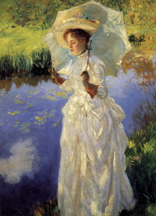 woman in a white dress and perisol walks by a pond