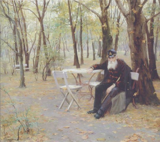man in dress blues sits at a table in the park with the trees barren