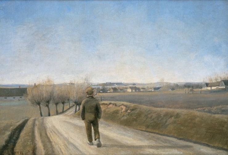 boy walks on a road with trees in the distance